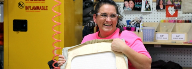  	A smiling female material handler holds a chair's seat.